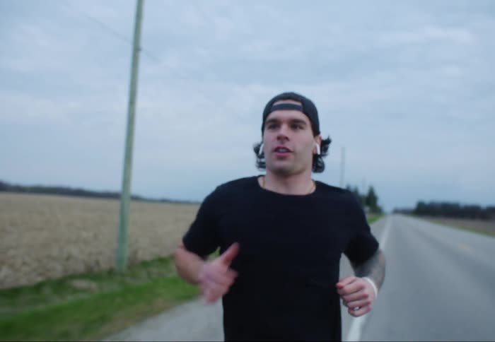 Man with a cap earphones and a black t-shirt jogs on a road in the countryside