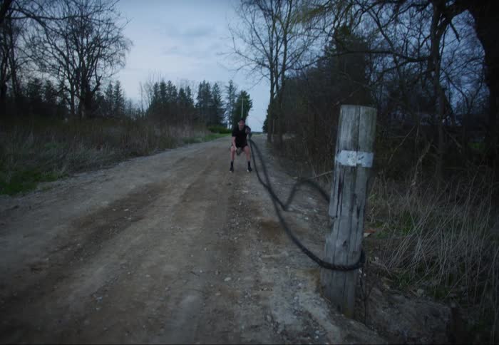 Man exercising with long ropes around wooden post on gravel road