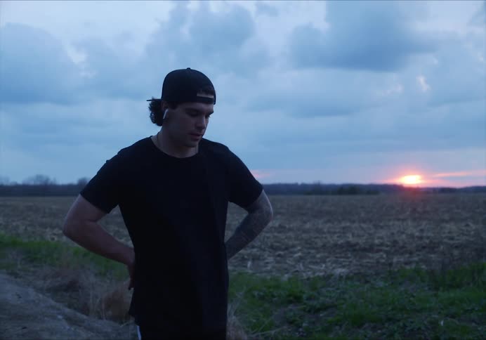A man wearing earbuds attempts to catch his breath while pacing on a dirt road at sunset