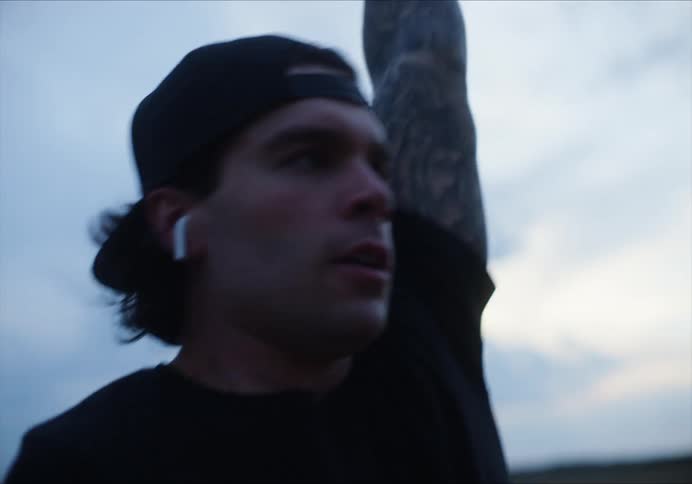 A teenage boy with airpods in lifts weights in a field
