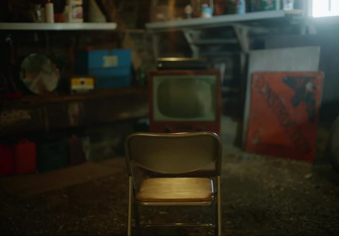 A metal folding chair sitting in front of an old fashioned television in an old shack with a dirt floor