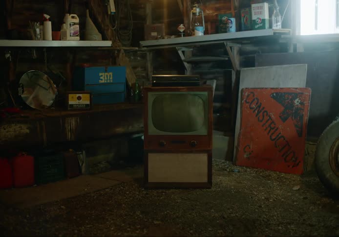Antique console television sits near other old items in a dusty garage