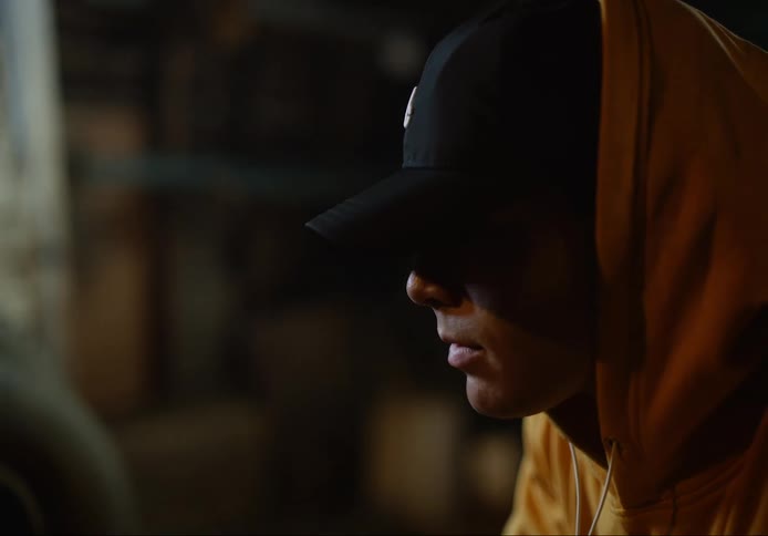 A young man sitting indoors with a hat and hoodie on
