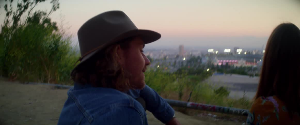 Young couple sits on overlook above city at dusk