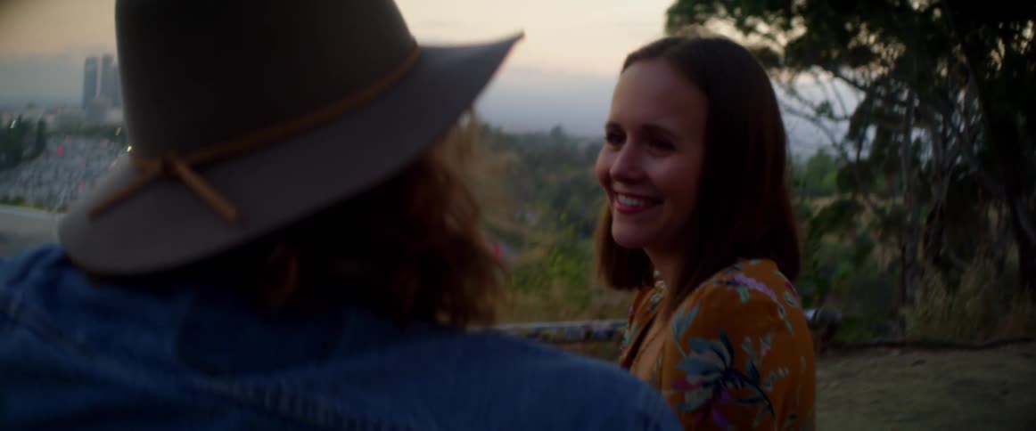 Man and woman laugh and talk on slight hill as fog obscures skyline in valley