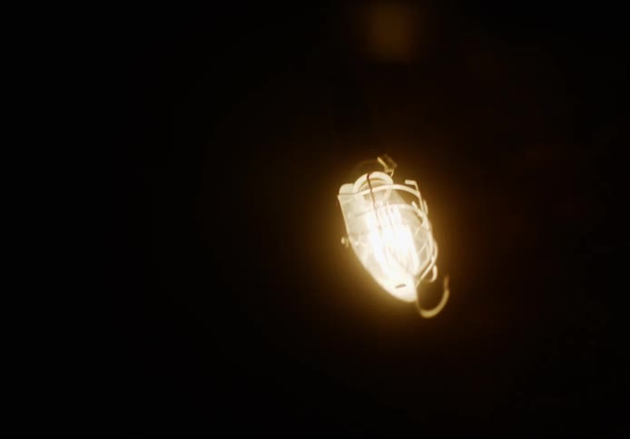 An inspection lamp lights up a dark unfinished room as it swings wildly