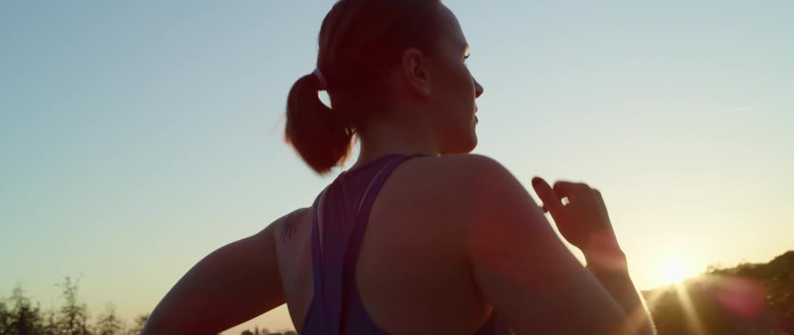 A woman jogs outdoors as the sun peaks over a distant hill