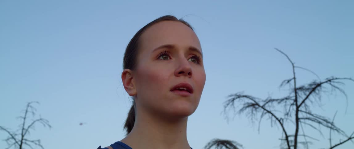 Woman with a ponytail breathes deeply and smiles slightly at dusk