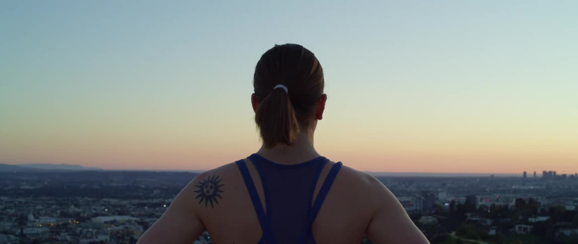 A woman with a pony tail stands and looks at the city skyline