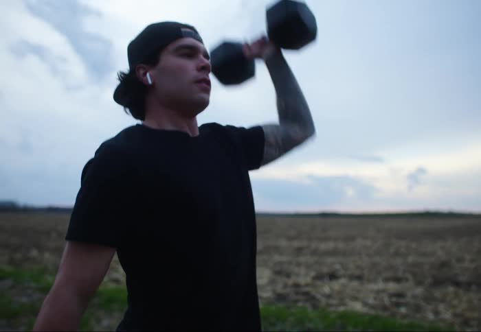 A man lifts a weight in his arm up and down while standing on a rural dirt road
