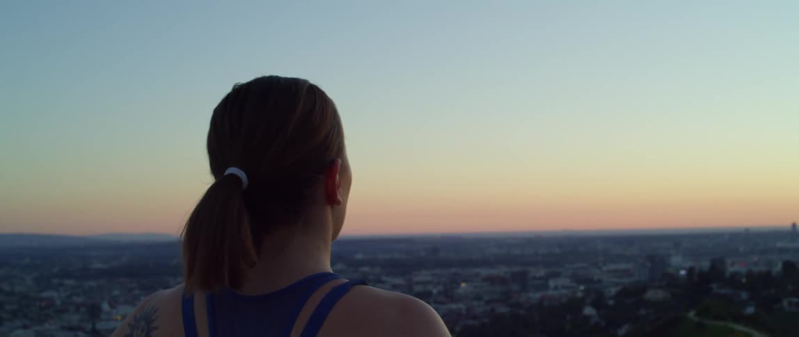 Female runner jogs and looks over the city from a hill at dusk