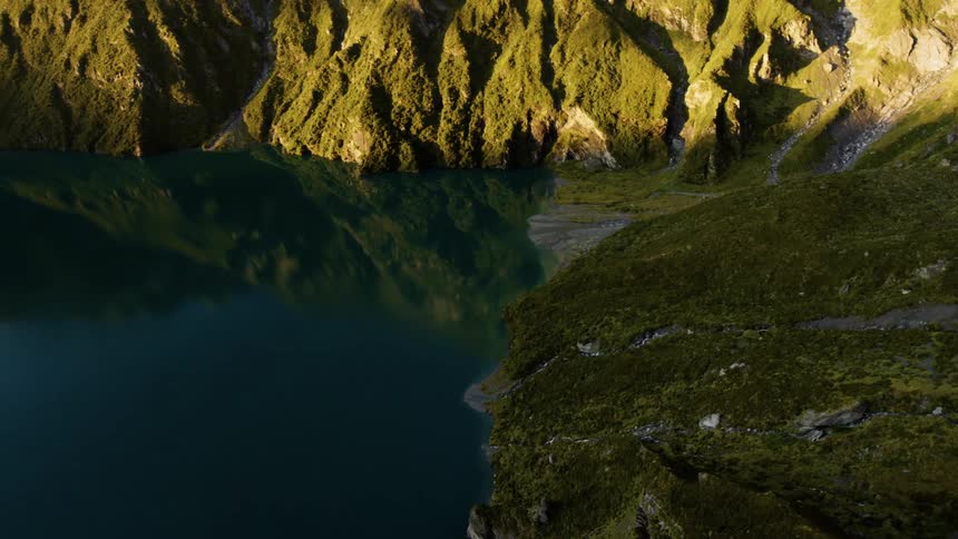 Still blue water reflects green craggy mountains