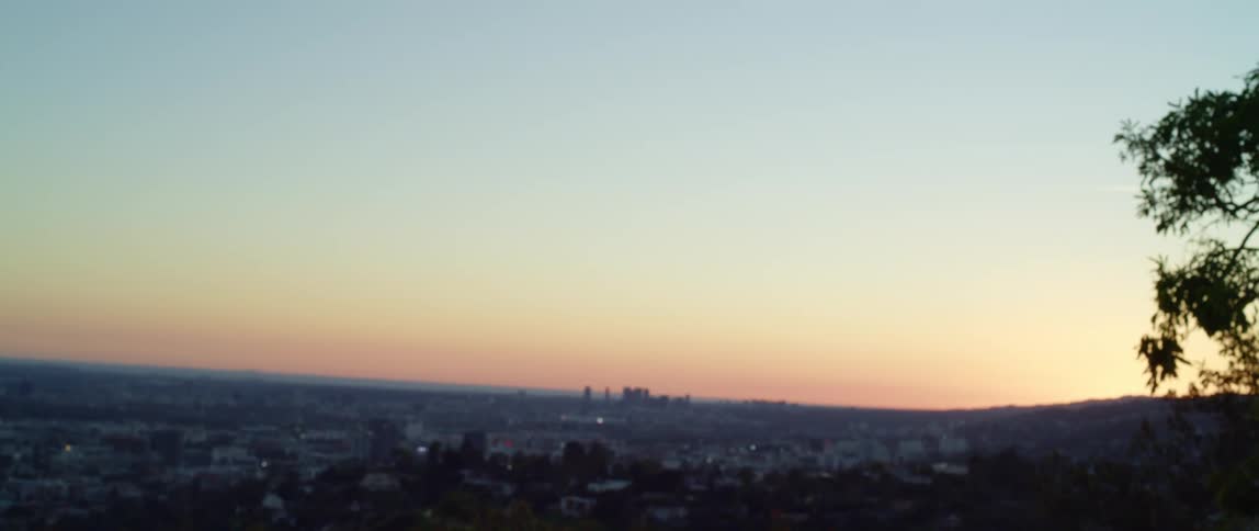 A woman looks out over a city from the hills bordering it before turning and jogging out of frame