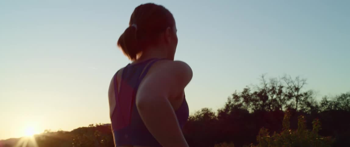 Woman with a ponytail sport bra and tights jogs on a dirt road at sunset