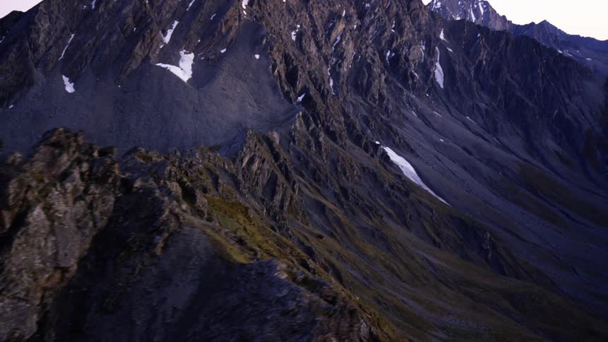 A stone mountain ridge covered in both sparse vegetation and snow
