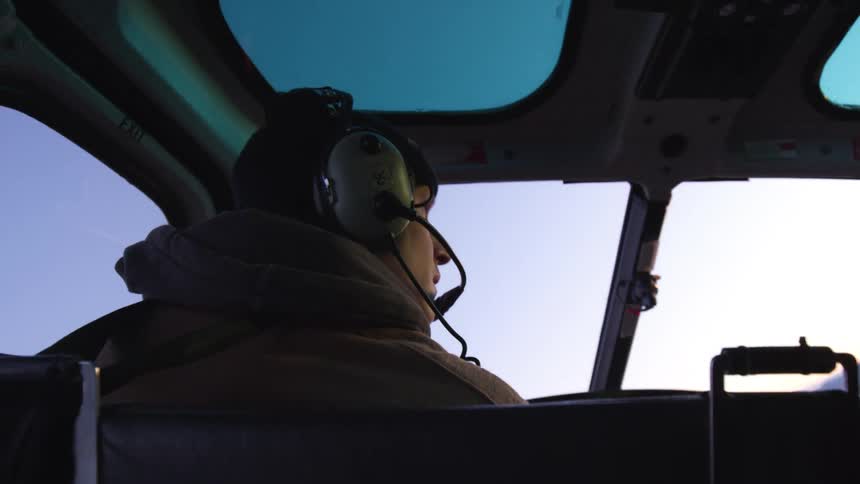 An interior view of a young man piloting a helicopter of a mountainous landscape