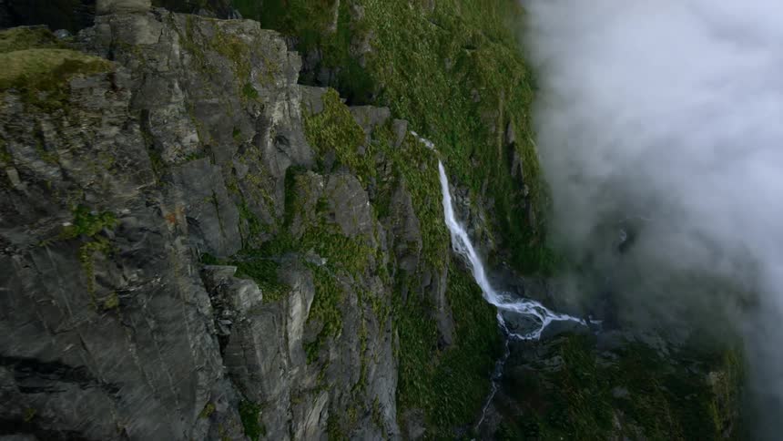 Water falls from a deep ravine on a mountain ridge onto a ledge shrouded in thick fog
