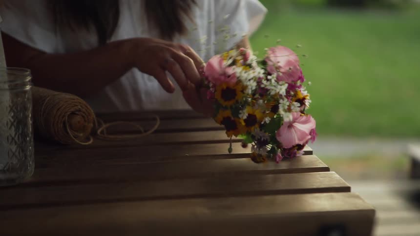 A woman sits at an outside table making a flower bouquet