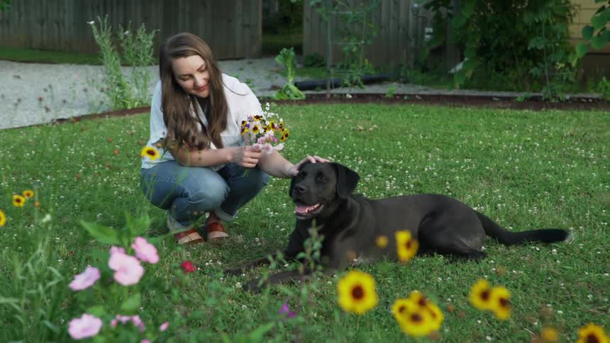 A woman is holding flowers and petting her dog