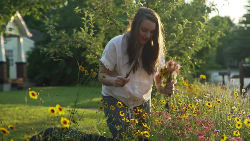 A woman shows a flower arrangement gathered from the yard of her house to a dog standing beside her