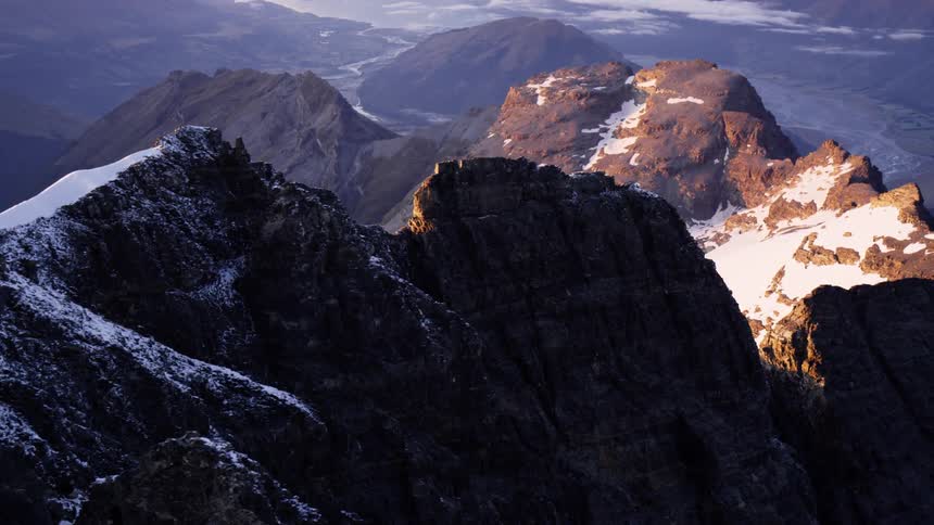 A stone mountain range covered in patches of snow in the evening