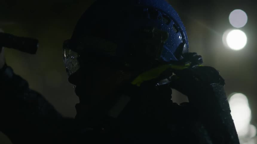 Person wearing goggles and a helmet uses flashlight in pouring water with spotlight providing extra light