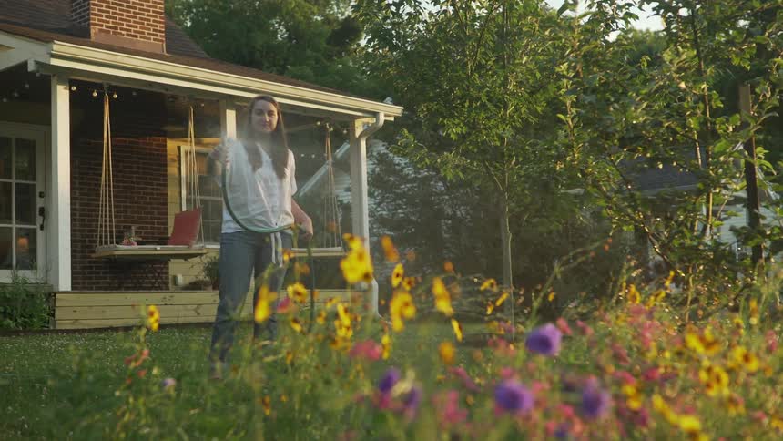 A woman waters flowers in her yard