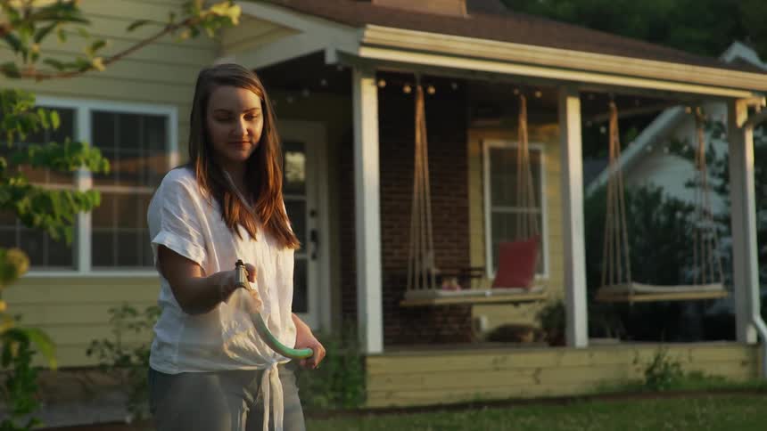 A teenage girl waters plants outside her home