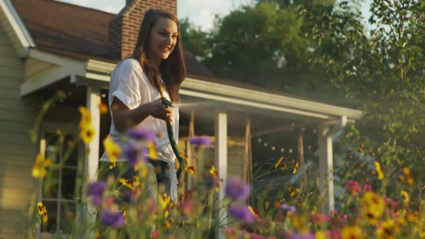 Young woman watering flower garden in early morning