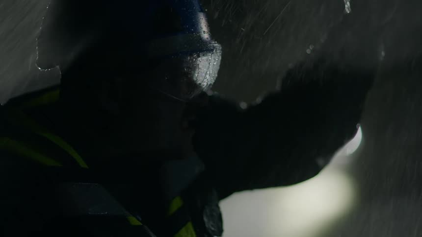 A man standing outside with a flashlight searching for something in the rain