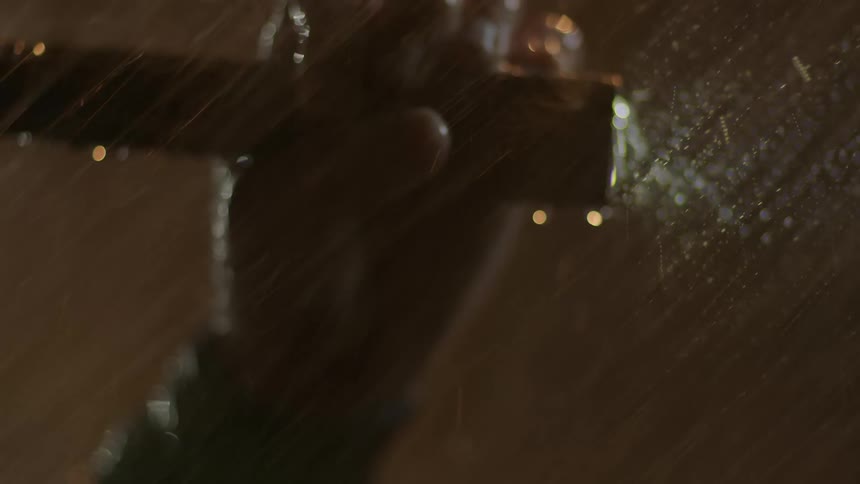 A person holds a flashlight under heavy rain at night