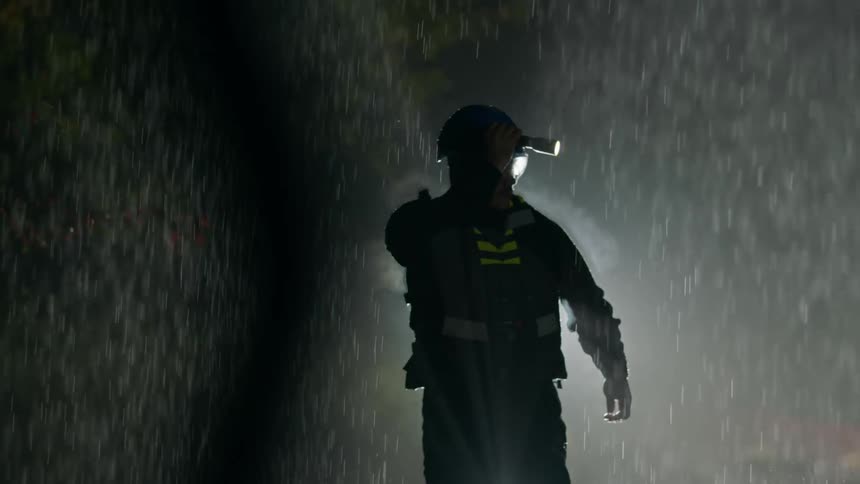 A man outside in the pouring rain searches with a flashlight