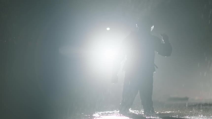 A first responder searches with his flashlight as he walks in a to a lake in the pouring rain