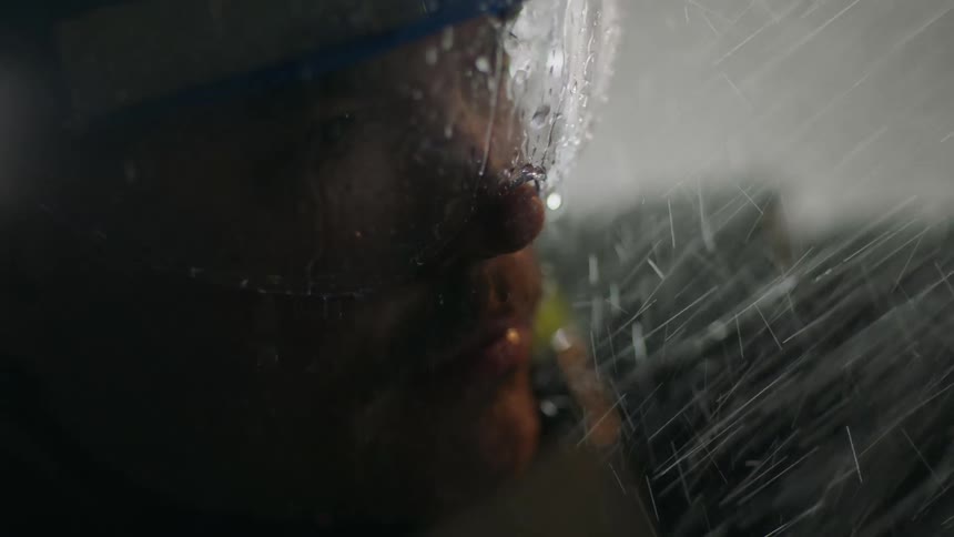 A man in safety equipment stands outdoors in heavy rain at night