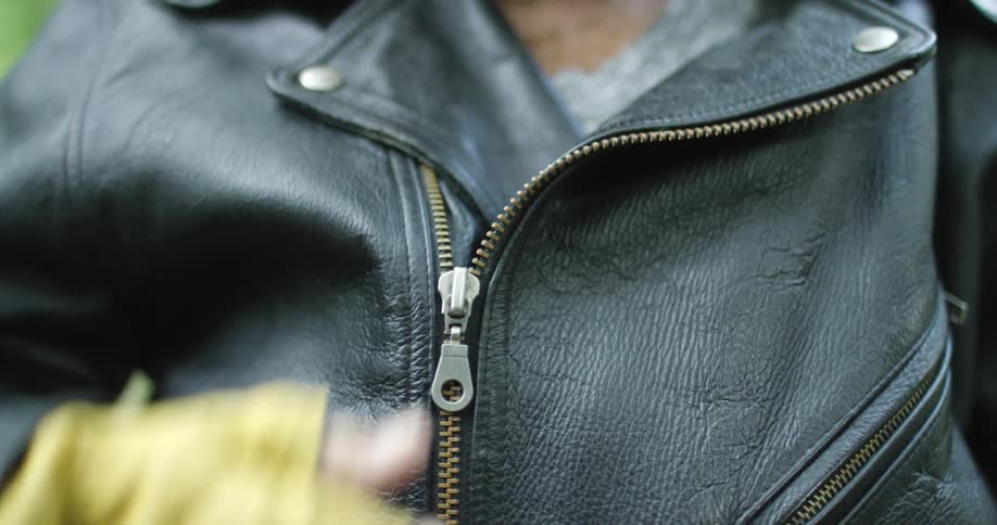 A woman wears yellow fingerless gloves as she zips up her black leather jacket