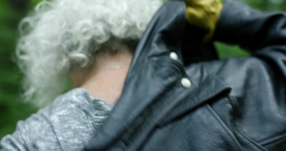 Elderly woman with grey hair puts on a leather jacket
