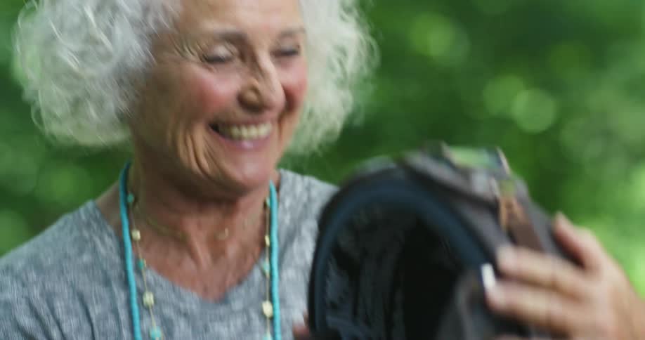 An elderly woman laughs while examining a retro motorcycle helmet