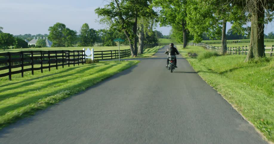 Man with a helmet and a leather jacket rides a motorcycle on a country road in the countryside