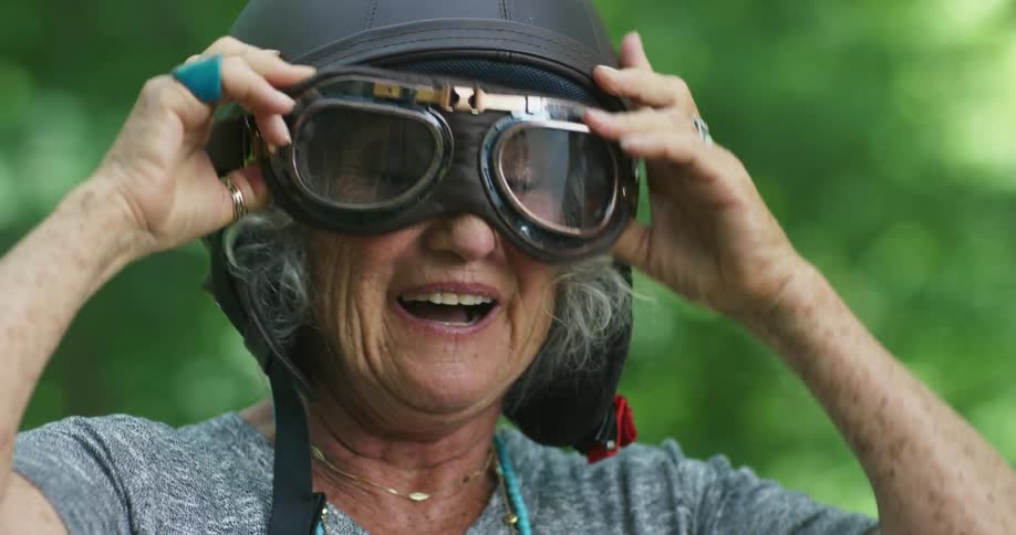 Elderly woman puts on a motorcycle helmet and goggles