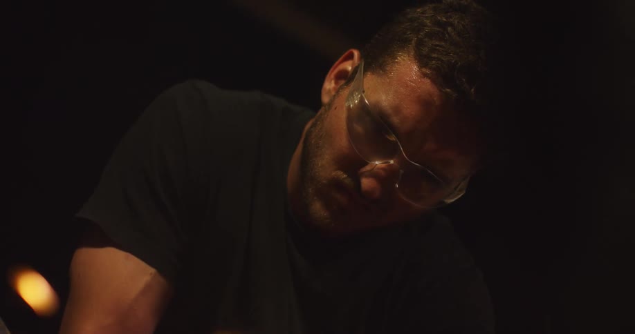 A young man in front of a fire looks down and concentrates
