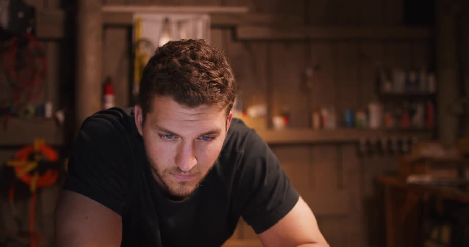 Man with a black t shirt and a beard looks at a laptop screen in a room