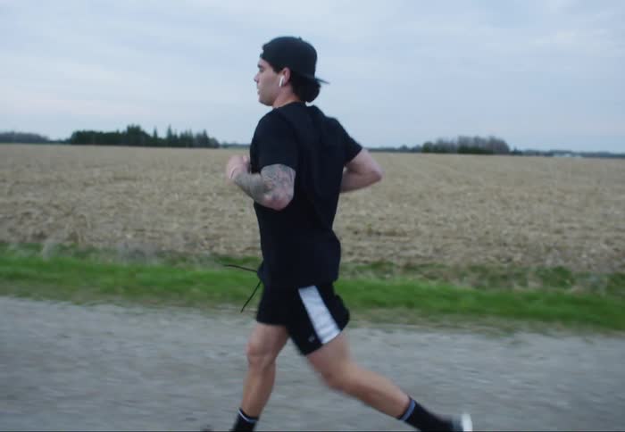 A man jogs on a dirt road near a field