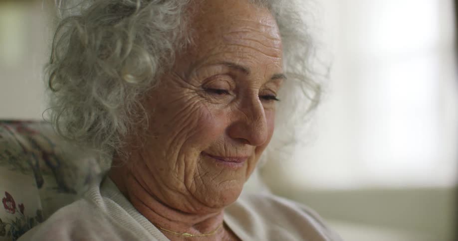 Elderly woman with grey hair and wrinkles reads a letter and smiles slightly