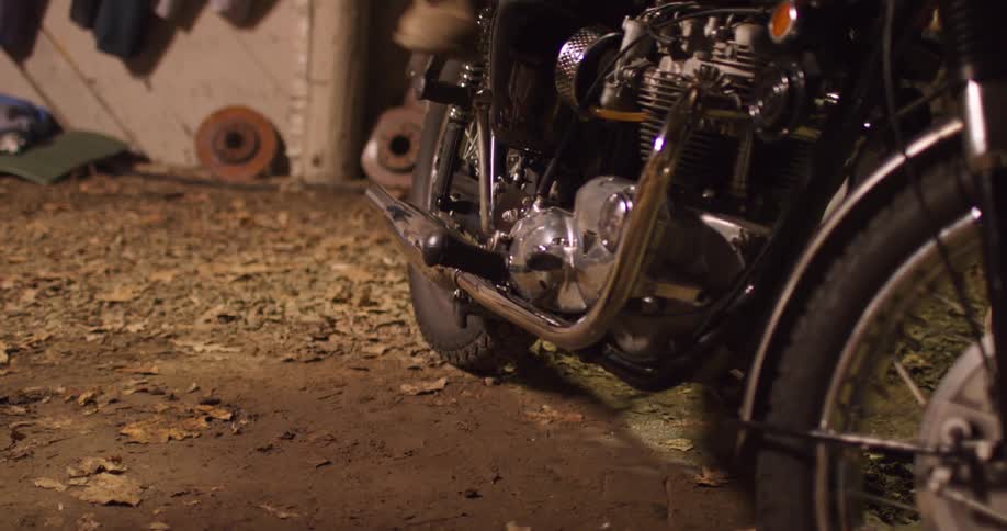 A person slams their foot down to start a motorcycle in a garage
