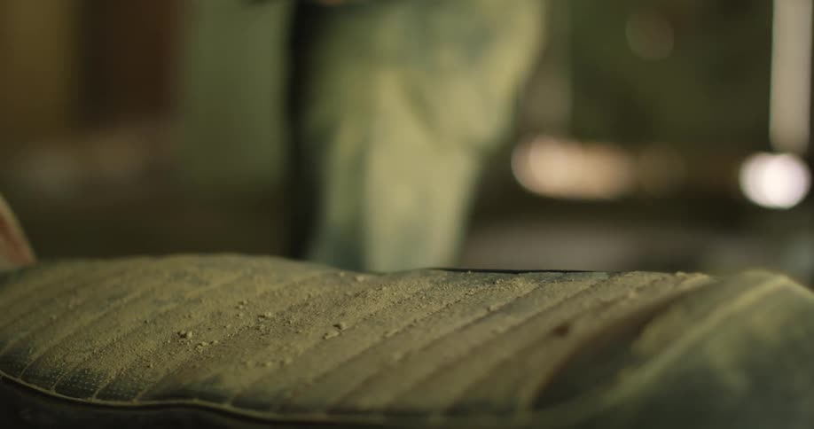 A man takes a cover off of a seat and blows dust off of it