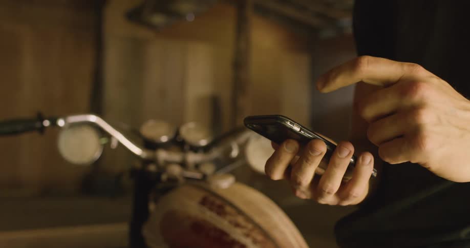 A man stands by his motorcycle and scrolls on his cell phone