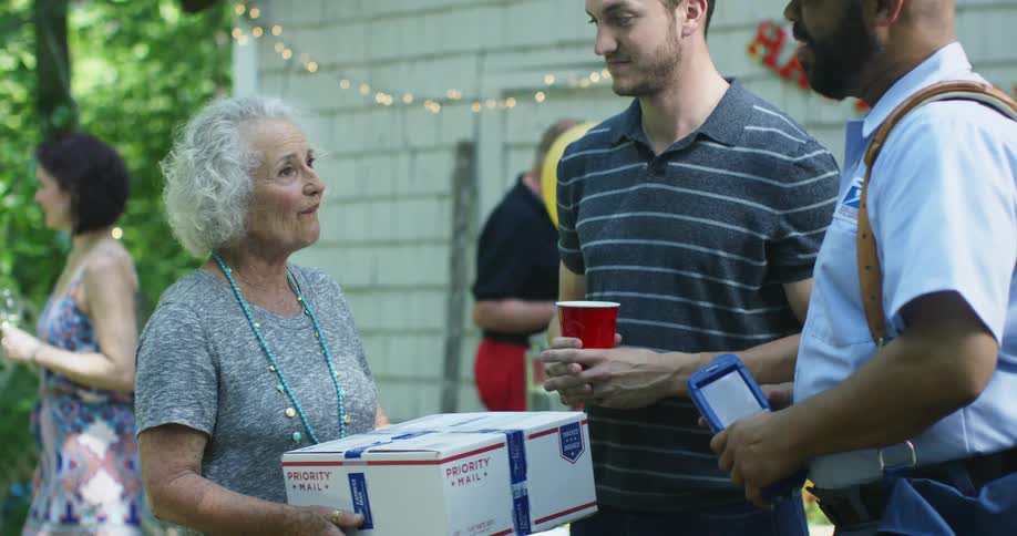 A postman handing a package to a woman and shaking a mans hand