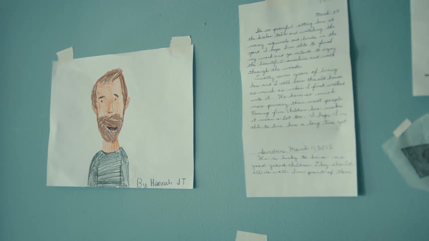 A handwritten letter and a drawing of a man are taped up and on display on a turquoise blue wall