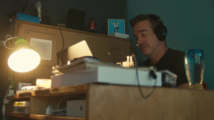 A man talks to someone on a headset while sitting at his desk and using a laptop