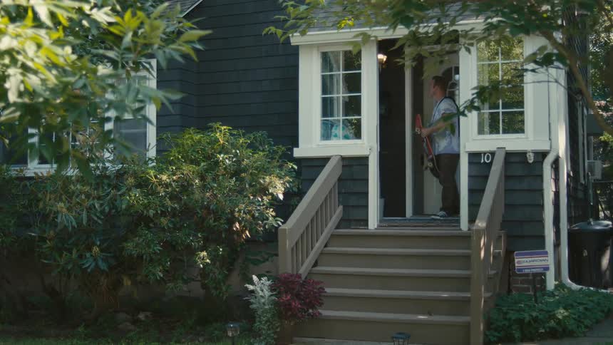 Man walks out of house and down steps carrying skateboard